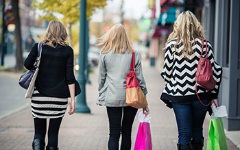 Three woman carrying shopping bags walk down a sidewalk.