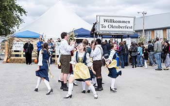 German dancers perform in front of a "welcome to Oktoberfest" sign.